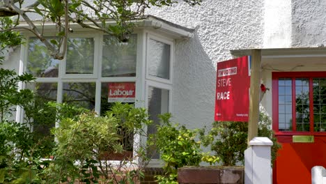 Signo-De-Trabajo-De-Votación-Fuera-De-Casa-Con-Jardín-Y-Ventanas,-Elección-En-El-Reino-Unido