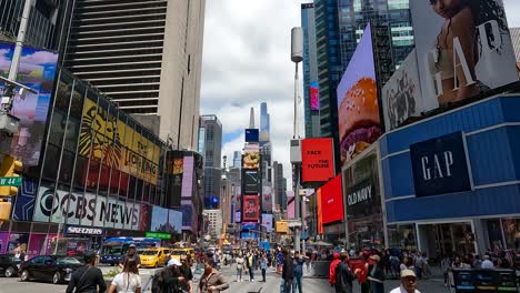 The-camera-tilts-upwards-from-the-busy-street-with-people-from-different-ethnic-groups-and-GAP's-entrance-to-the-tall-buildings-with-ad-screens-in-Times-Square