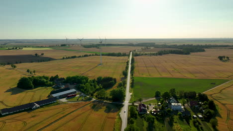 Aerial-view-of-wind-turbines-in-golden-fields,-with-a-rural-road-leading-towards-the-horizon,-capturing-the-integration-of-agriculture-and-green-energy