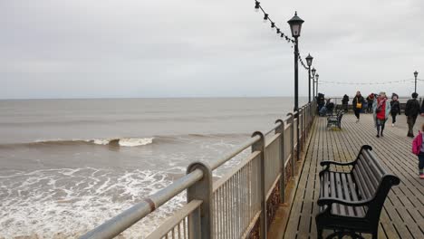 People-walking-on-the-Pier-at-Skegness-on-a-grey-day-with-Victorian-lamppost-lantern-lights