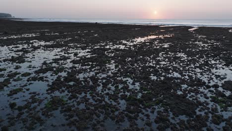 Low-Angle-Drone-shot-moving-over-Bingin-Beach-low-tide-reef-with-sunset-in-Uluwatu-Bali-Indonesia