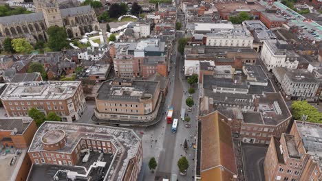 Drone-tracking-shot-of-a-bus-navigating-the-bustling-high-street-in-Exeter,-Devon,-UK