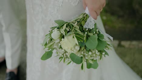 Bride-holding-a-bouquet-of-white-flowers-and-greenery,-showcasing-wedding-elegance