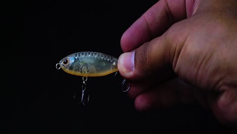 Hand-holding-artificial-lure-of-mini-minnow-with-black-background