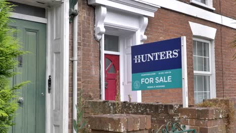 For-Sale-estate-agent-sign-outside-colorful-front-doors-of-terraced-houses,-capturing-housing-market,-Exeter-Devon-UK,-June-2024