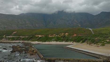 Drone-revealing-seagulls-flying-above-an-empty-tidal-pool-near-Cape-Town,-South-Africa