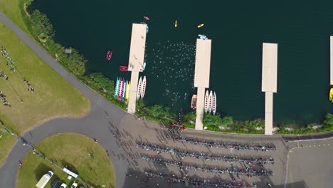 Top-still-shot-of-Triathlon-at-Dorney-lake,-triathletes-running-on-the-track-and-swimming-towards-the-transition-area