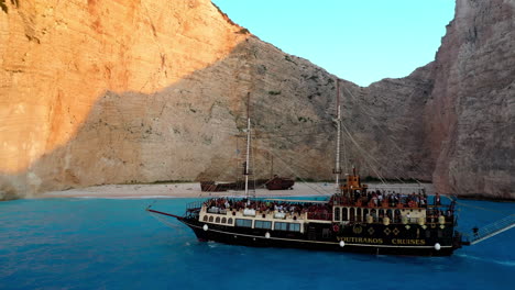 Aerial-footage-of-Navagio-Beach-with-a-cruise-ship-full-of-tourists-in-the-foreground