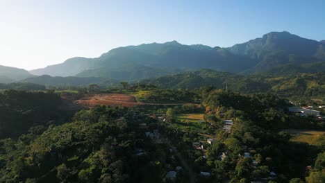 Vista-Aérea-De-Un-Paisaje-Montañoso-Y-Exuberante-Durante-El-Día,-Que-Muestra-Vegetación,-Colinas-Y-Pequeños-Asentamientos.