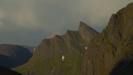 Sun-casting-a-golden-hue-and-rainbow-over-the-rugged-peaks-of-Husfjellet-in-Senja,-Norway