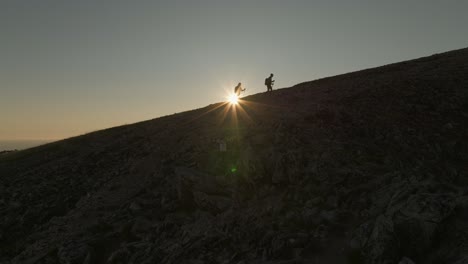 Young-couple-trekking-up-Husfjellet-in-Senja,-Norway,-during-a-stunning-midnight-sun-sunset