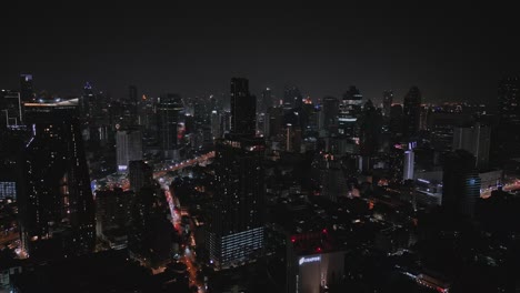 Buildings-And-Skyscrapers-In-Downtown-Bangkok,-Thailand-At-Night---Aerial-Drone-Shot