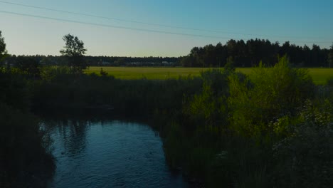 Beautiful-footage-of-a-rural-lake-or-a-stream-in-Tallinn-Estonia-during-a-sunset-and-sundown-with-clear-skies-and-green-fields-in-the-background-with-tree-line-as-a-silhouette-in-4K