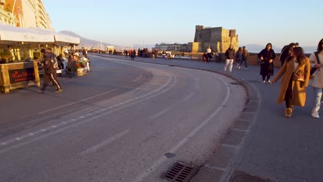 Menschen,-Die-Bei-Sonnenuntergang-Auf-Der-Via-Partenope-Spazieren-Gehen,-Mit-Castel-Dell&#39;Ovo-Im-Hintergrund---Italien