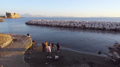 People-enjoying-along-the-waterfront-at-the-gulf-Of-Naples-with-Castel-dell'Ovo-in-the-background---Italy