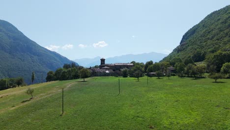 Eine-Von-Einem-Hohen-Aussichtspunkt-Aufgenommene-Ruhige-Luftlandschaft,-Die-Ein-Zwischen-Grünen-Bergen-Eingebettetes-Dorf-An-Einem-Klaren-Tag-Zeigt