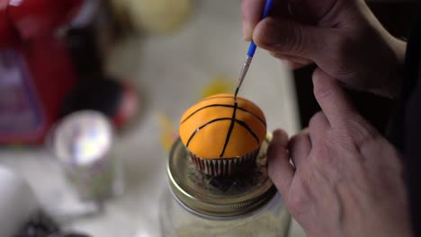 Close-up-on-woman's-hands,-painting-a-cupcake-as-a-basket-ball,-with-blurred-background,-static-4k-shot