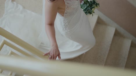 Bride-ascending-stairs,-holding-the-handrail,-showcasing-her-elegant-wedding-dress