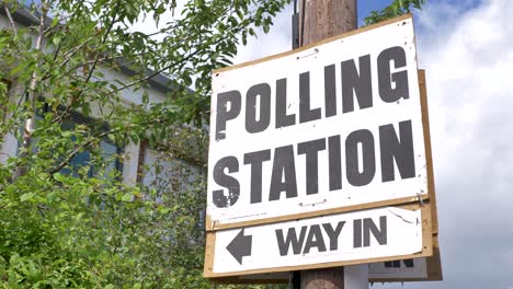 Polling-station-sign-on-post-with-greenery-indicating-way-in,-UK-election