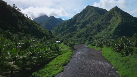 River-Valley-towering-mountain-volcano-peaks-Teahupoo-town-Tahiti-French-Polynesia-Moorea-Papeete-aerial-drone-stunning-island-late-morning-afternoon-blue-sky-daytime-sunny-clouds-forward-pan-up