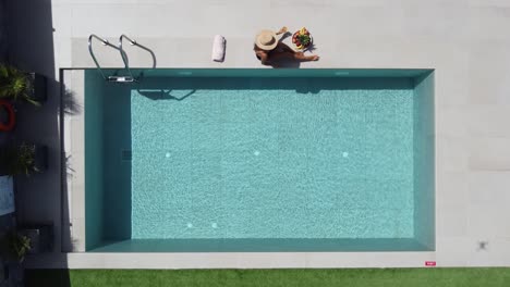 Dark-haired-slim-woman-lying-at-the-edge-of-a-beautiful-outdoor-pool---she-wears-a-dark-swimming-suit-and-enjoys-the-sun