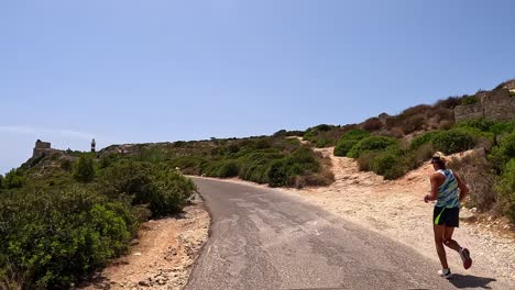 Two-people-jogging-along-secluded-sloping-roadside,-point-of-view-journey