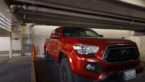 A-man-and-woman-enter-a-parking-garage-and-walk-past-large-red-pickup-truck