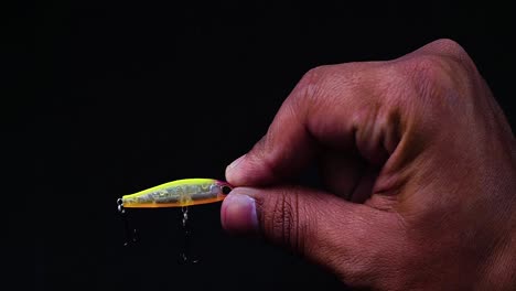 Hand-holding-artificial-lure-of-mini-minnow-with-treble-hook-installed-on-black-background