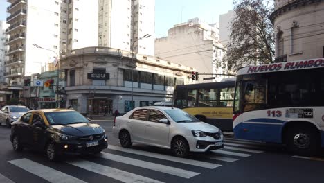 Establecimiento-En-El-Barrio-De-Flores,-Tráfico-De-La-Ciudad-De-Buenos-Aires,-Argentina,-Avenida-Rivadavia-A-La-Luz-Del-Día,-Autobuses,-Coches-Y-Taxis-Circulando.