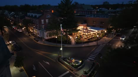 Aerial-approaching-shot-of-center-square-of-american-town-with-american-flag-and-cars-in-road