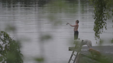 Boy-Enjoying-Summer-in-Finland:-Fishing-in-Lake-with-His-Dogs,-Slow-Calm-Lifestyle