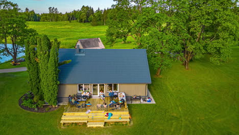 Adults-Enjoying-a-Small-Gathering-on-the-Porch-of-a-House-Set-on-a-Grassy-Area,-Surrounded-by-Trees---Timelapse