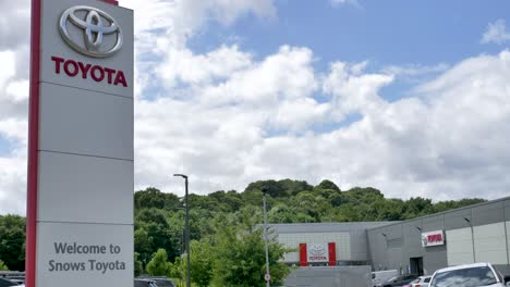 Toyota-Logo-Und-Beschilderung-Außerhalb-Des-Autohauses-Mit-Viel-Grün-Und-Blauem-Himmel,-Exeter,-Devon,-Großbritannien,-Juni-2024