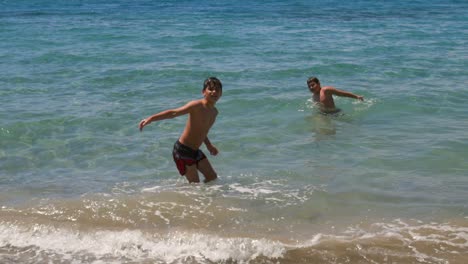 Slow-motion-100fps-shot-of-two-caucasian-brothers,-enjoying-the-sea-of-Kalamata,-Peloponnese,-Greece,-playing-around-in-the-seashore