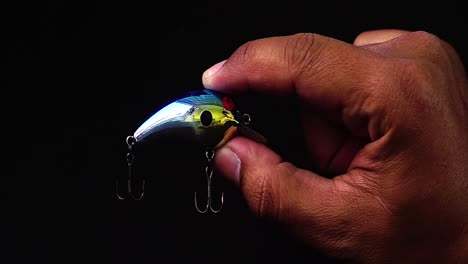 Hand-holding-artificial-lure-of-mini-minnow-with-treble-hook-installed-on-black-background