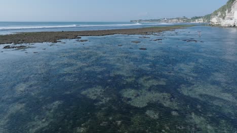 Low-angle-drone-shot-of-low-tide-reef-and-waves-in-Uluwatu-Bali-Indonesia