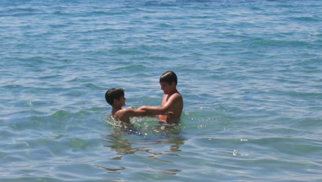 Caucasian-brothers-share-a-hug-and-splashing-each-other-in-the-sea,-medium-100fps,-slow-motion-footage