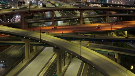 Nighttime-aerial-drone-footage-of-a-multi-level-freeway-interchange-in-downtown-American-city-showcasing-the-intricate-network-of-overpasses-and-lit-up-roads