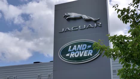 Jaguar-Land-Rover-logo-on-sign-outside-of-dealership-with-cloudy-sky,-Exeter,-Devon,-UK,-June-2024