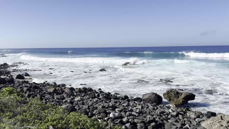 A-scenic-view-of-the-rocky-shoreline-of-Oahu,-Hawaii,-with-waves-crashing-against-the-rocks-under-a-clear-blue-sky,-capturing-the-island's-natural-beauty-and-the-power-of-the-Pacific-Ocean