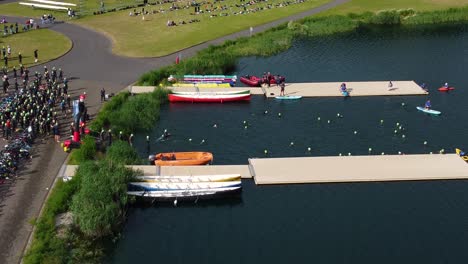 Toma-De-Drones-De-Triatlón-En-Dorney-Lake,-Los-Triatletas-Comienzan-La-Carrera-Y-Nadan-Hacia-El-área-De-Transición.