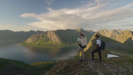 Young-couple-hiking-at-sunset-on-Norway's-Senja-Husfjellet-mountain-with-a-stunning-view-of-the-fjord