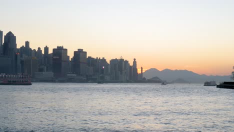 City-skyline,-silhouettes-of-tall-buildings,-water-ripple,-ferry-vessel