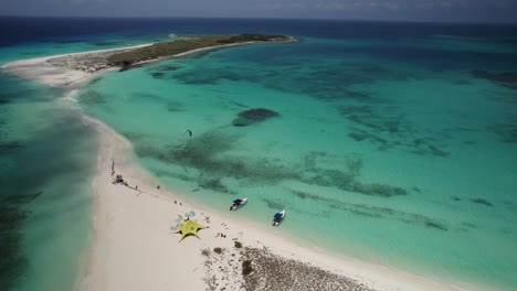 Cayo-de-agua-island-with-turquoise-waters,-sandy-beach,-and-boats-near-the-shore,-aerial-view