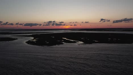 Aerial-dolly-to-setting-sun-as-ocean-water-ripples-across-Chincoteague-Island-Virginia,-slow-motion