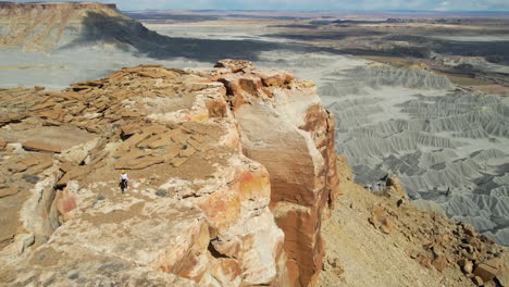 Vista-Aérea-De-Una-Mujer-Solitaria-Caminando-Sobre-La-Mesa-Cerca-Del-Borde-Del-Acantilado-Sobre-Las-Tierras-Baldías-De-Utah,-EE.UU.