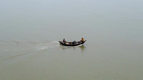 Aerial-tracking-of-a-small-fishing-trawler-boat-at-sea-with-three-men-sailing-along-the-coast-in-Bangladesh,-India