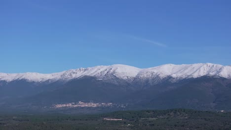 Filmando-Con-Un-Drone-De-167mm-En-El-Valle-Del-Tiétar-Donde-Vemos-El-Sistema-Central-De-Montañas-De-La-Península-Ibérica,-Las-Cimas-Están-Nevadas-Y-En-La-Ladera-Está-El-Pueblo-De-Piedralaves