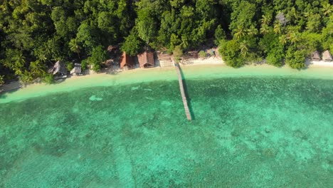 Aerial-view-of-a-beachfront-resort-on-Kri-Island-in-Raja-Ampat,-Indonesia,-showcasing-its-turquoise-waters-and-dense-forest