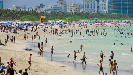 Miami-Beach,-Florida,-Con-Mucha-Gente-En-El-Agua-Y-Arena-Repleta-De-Sombrillas